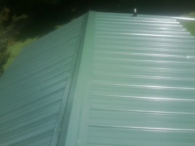 New green metal panels meeting at the ridge of a roof — Flat Roof Repair work by our crew in Glenville