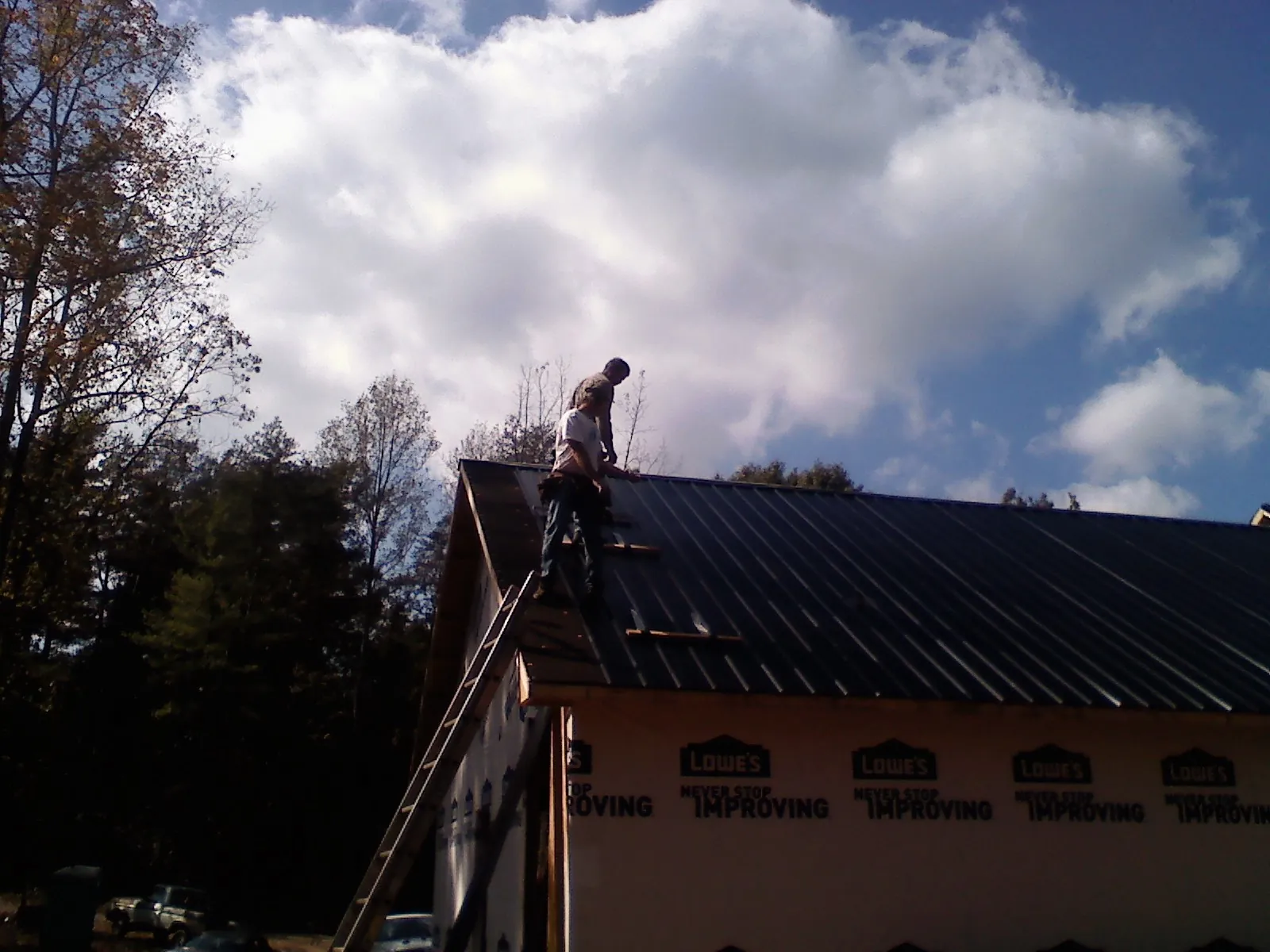 Roofer fastening dark metal panels high against a cloudy sky, from a Roof Inspection job in Glenville