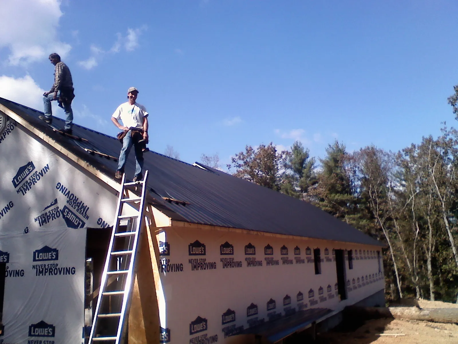 Two roofers standing on a long dark metal roof over a wrapped building in Glenville